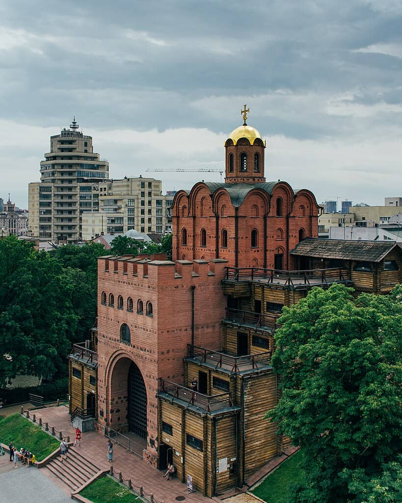 Історична церква з червоної цегли на фоні сучасних будівель Києва.