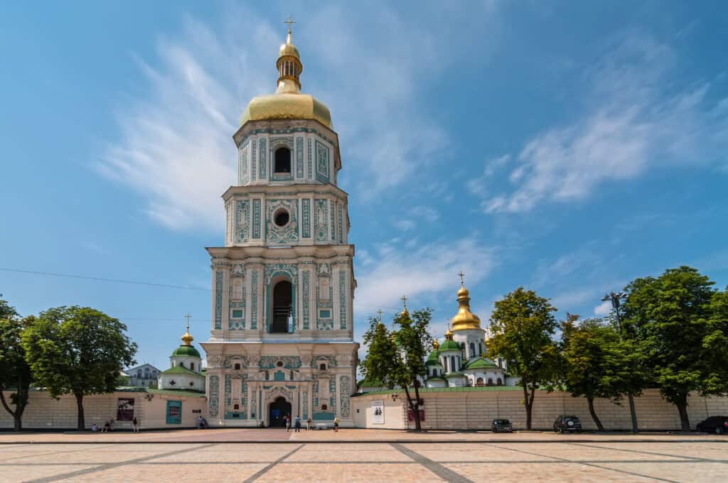 Барокова церква з високою дзвіницею на фоні неба та зелених дерев.