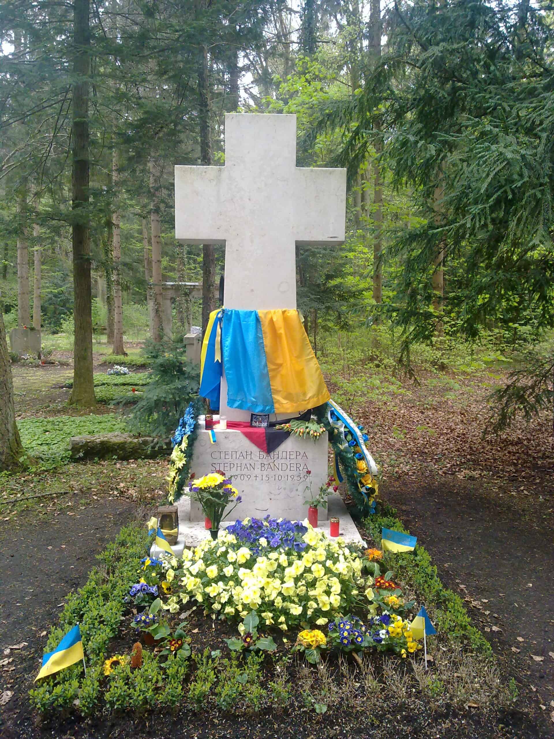 Меморіал Степану Бандері в лісі з квітами та українською символікою.