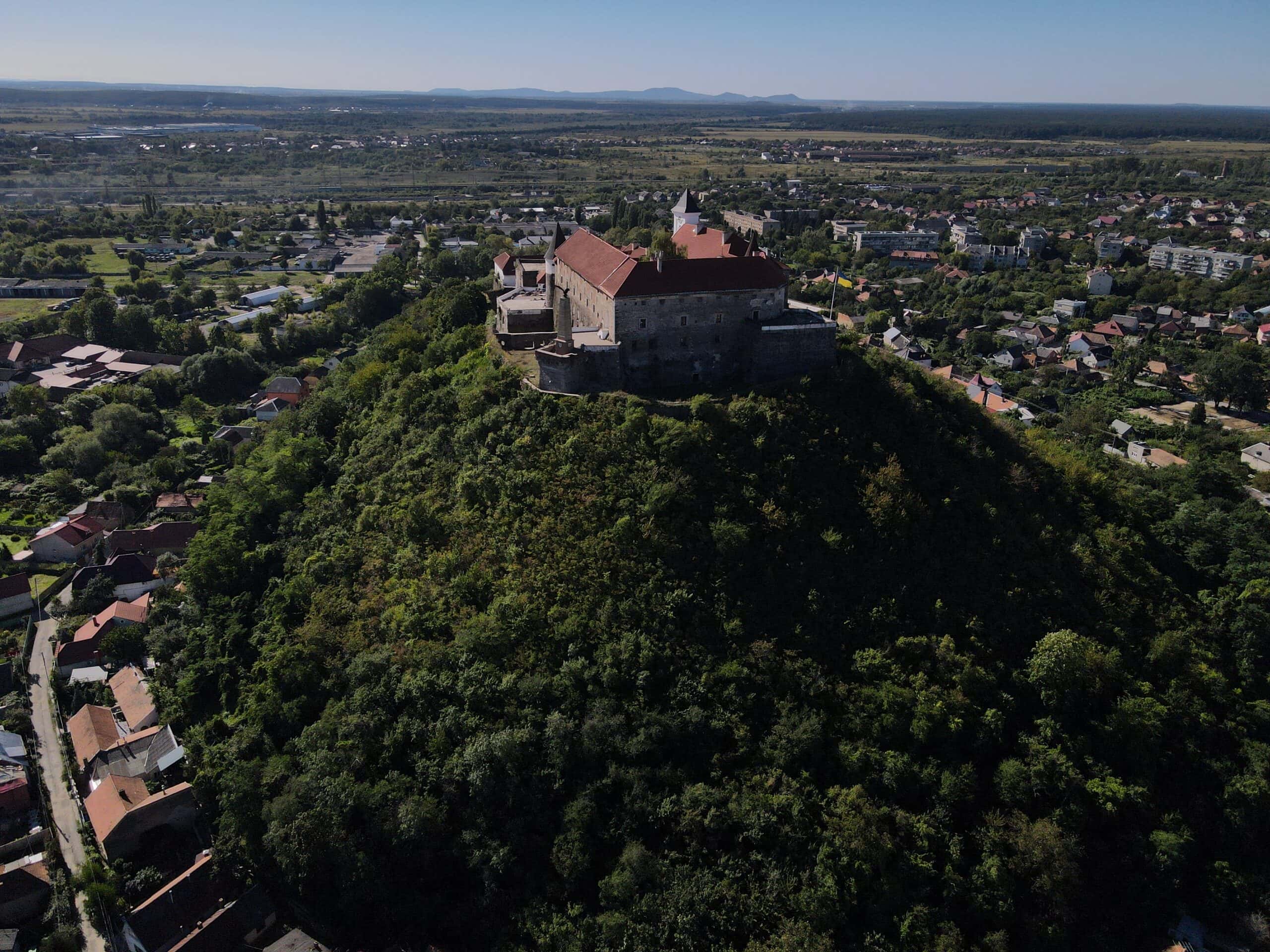 Замок на вершині пагорба з панорамним видом на місто і природу.