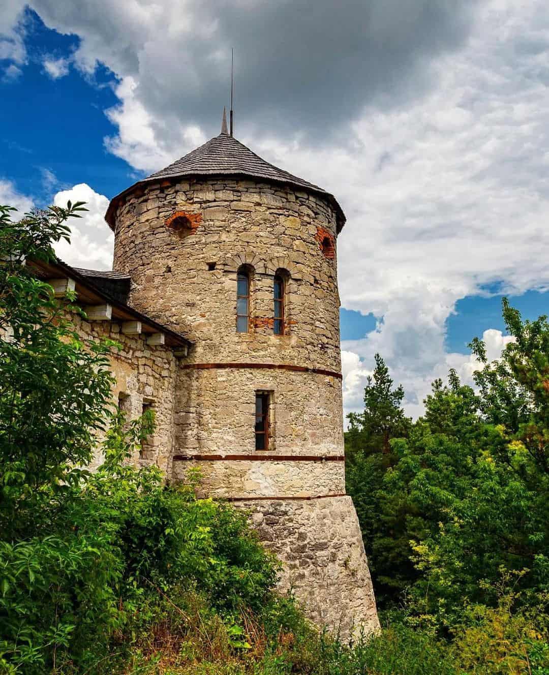 Старовинна вежа з каменю серед зелені та хмарного неба.