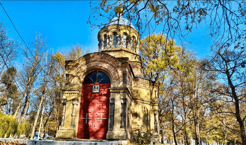 Старовинна церква в парку з деревами та яскравим небом.