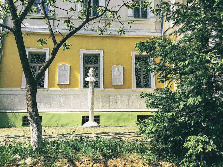 Фасад історичної будівлі з скульптурою та зеленню навколо.