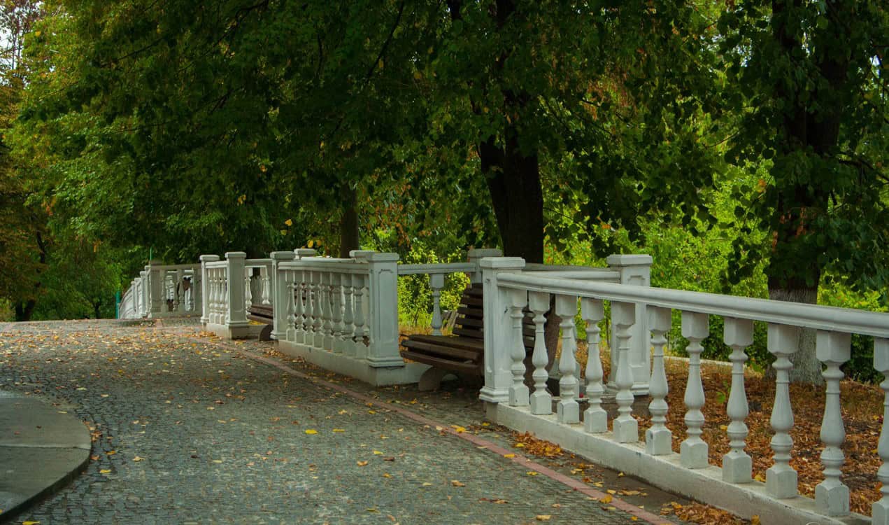 Містка огорожа з білого каменю на паркувальній доріжці з зеленим деревом на задньому плані.