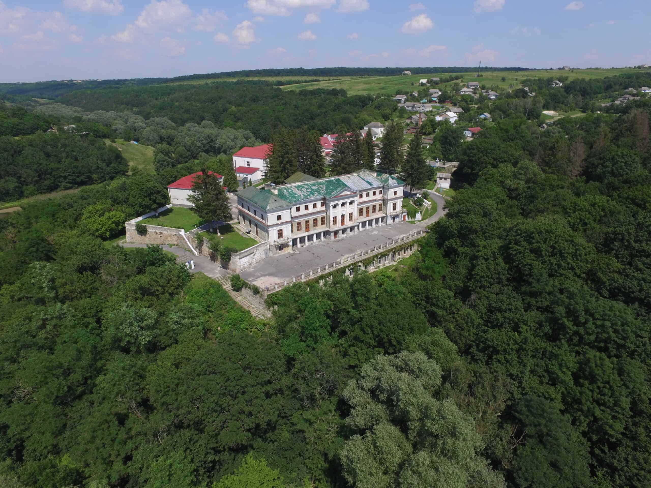 Палац у Мурованих Курилівцях на тлі зелених лісів і сільської місцевості.