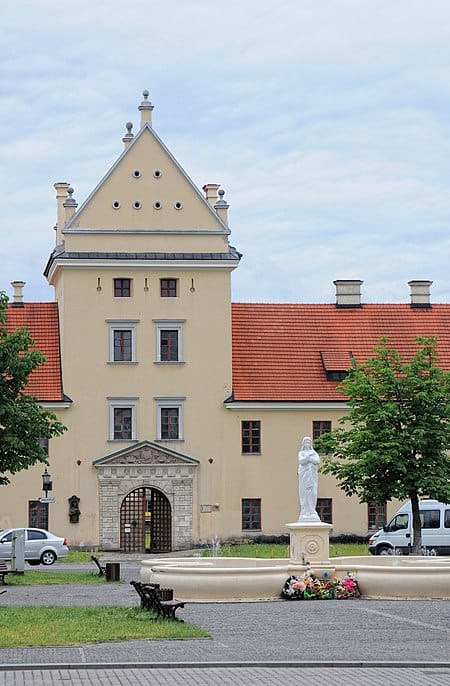 Жовківський замок з історичним фасадом і пам'ятником у передньому плані.