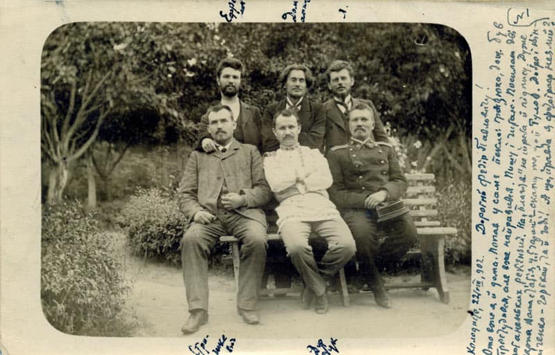 Групова фотографія з п'ятьма чоловіками на лавці та стоячими позаду, старовинне фото.