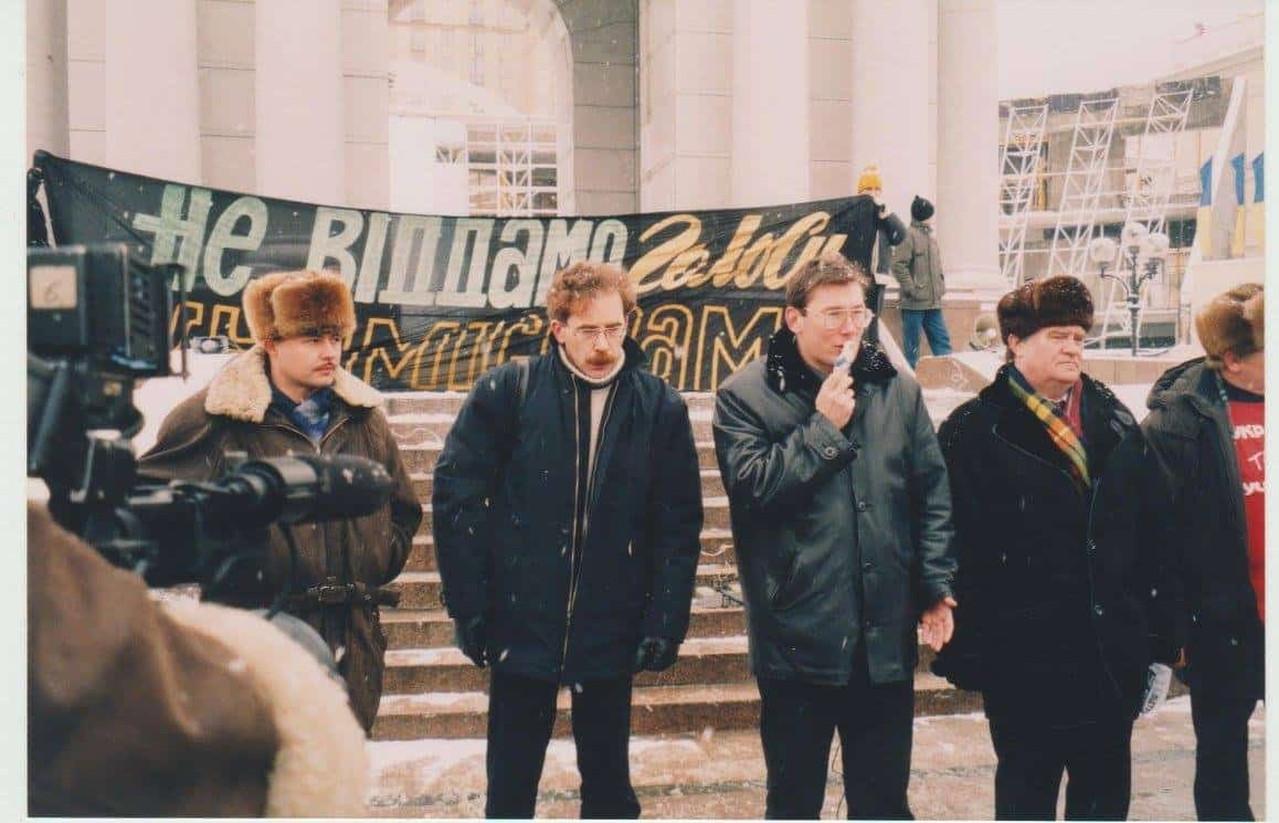 Мітинг під час акції «Україна без Кучми» біля будівлі з плакатом і людьми в зимовому одязі.