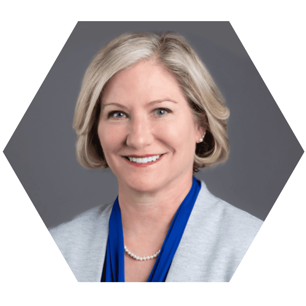 Ingrid Schunder a confident woman with blonde hair, wearing a light gray blazer, pearl necklace, and blue scarf, set against a neutral gray background.