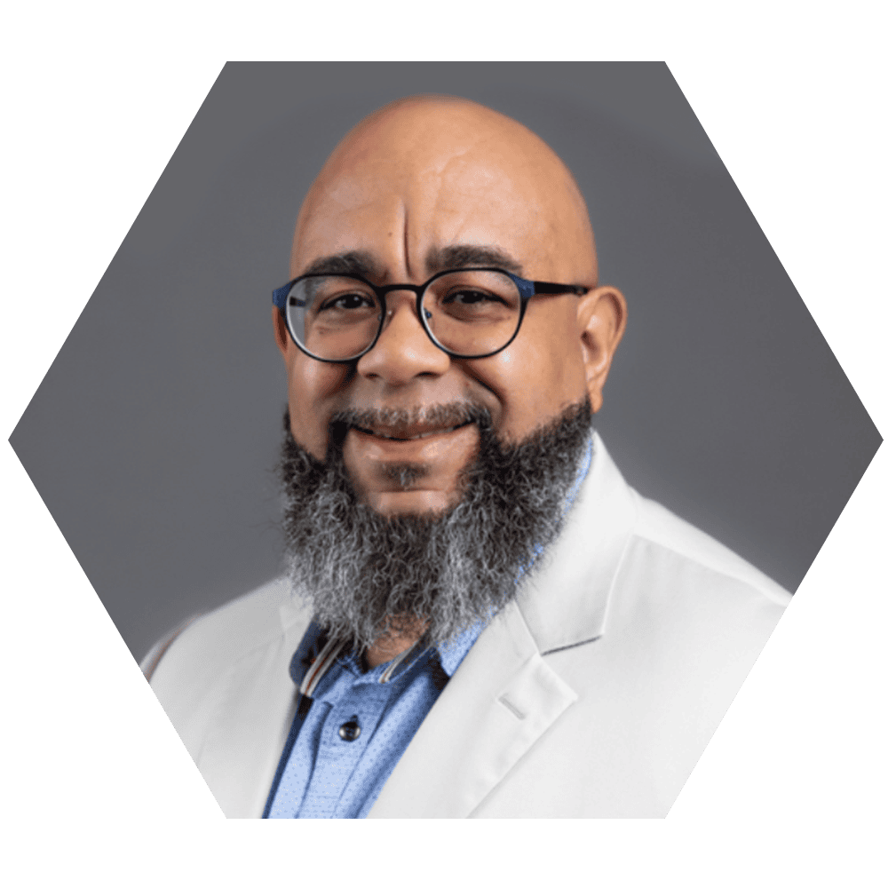 A professional portrait of Mike Tramber, smiling medical expert with glasses and a beard, dressed in a white coat against a neutral gray background.