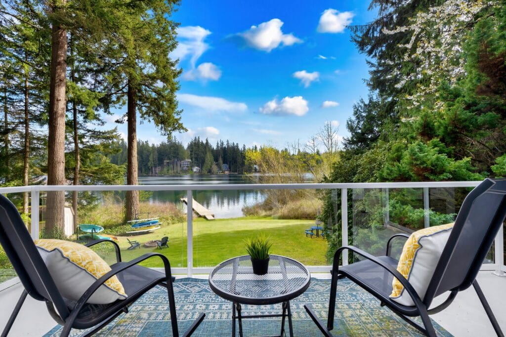 Tranquil lakeside view from a balcony with outdoor seating and lush green landscape.