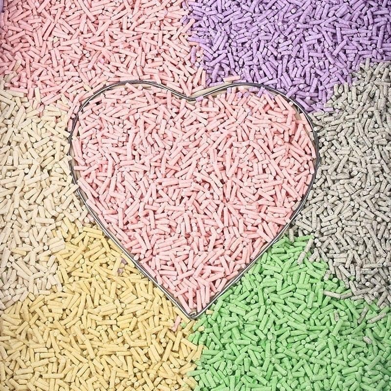 Colorful eco cat litter pellets in pink, green, yellow, purple, and grey with metallic heart outline.