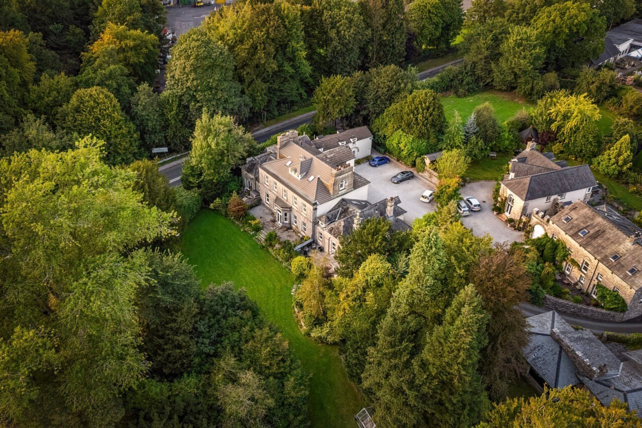 Aerial view of a historic stone mansion surrounded by lush green trees and gardens in the countrysid.