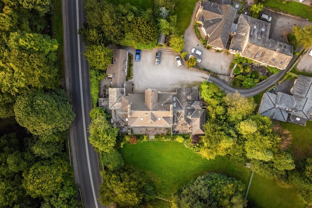 Aerial view of a residential property with surrounding greenery and parking area.