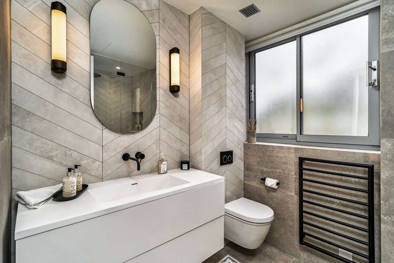 Modern bathroom with wall-mounted sink, mirror, and heated towel rail, natural light from window.