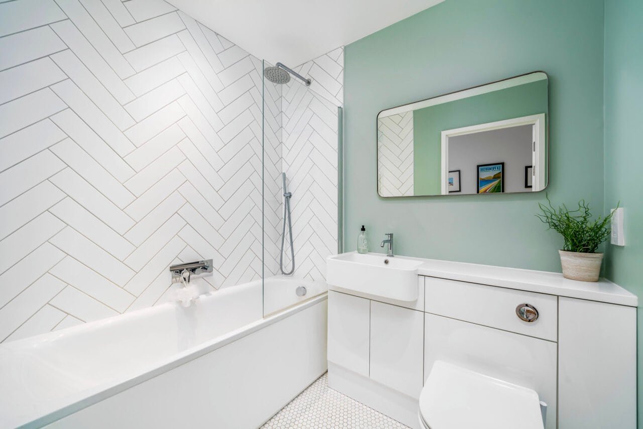 A modern bathroom with a white bathtub, green wall, and minimalist decor.