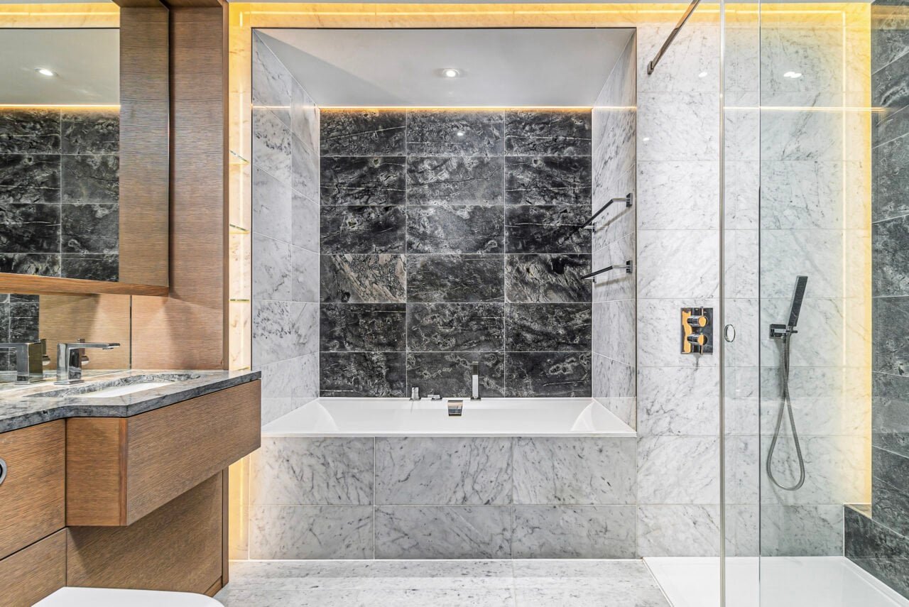 A modern bathroom with a white bathtub, black and white marble tiles, and glass shower enclosure.