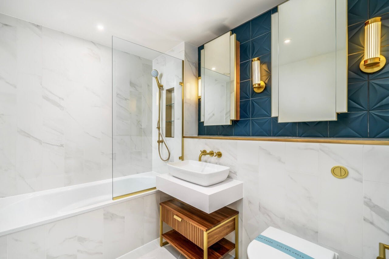 A modern bathroom with white marble walls, gold fixtures, and blue accent wall tiles.