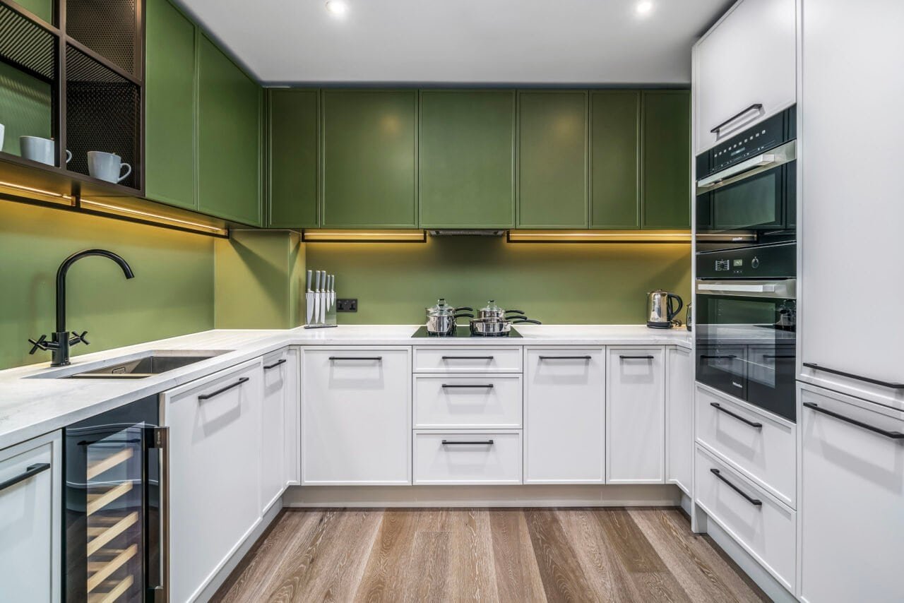 Modern kitchen with green and white cabinets, built-in appliances, and wooden flooring.