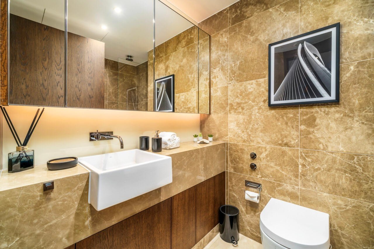 A modern bathroom with beige marble walls, a white sink, and a framed architectural photo.