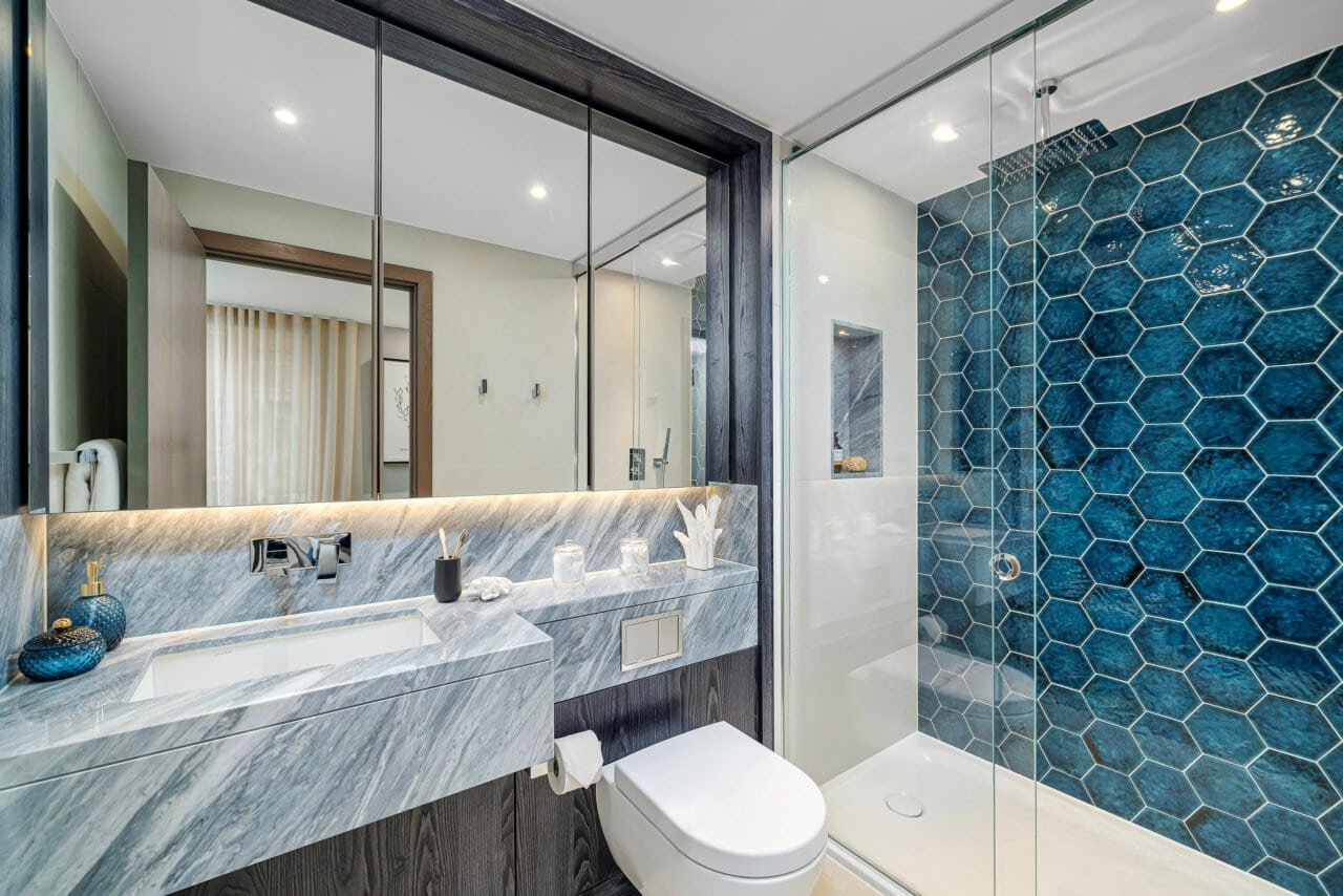 A modern bathroom with a marble vanity, large mirror, and a glass-enclosed shower with blue hexagona.