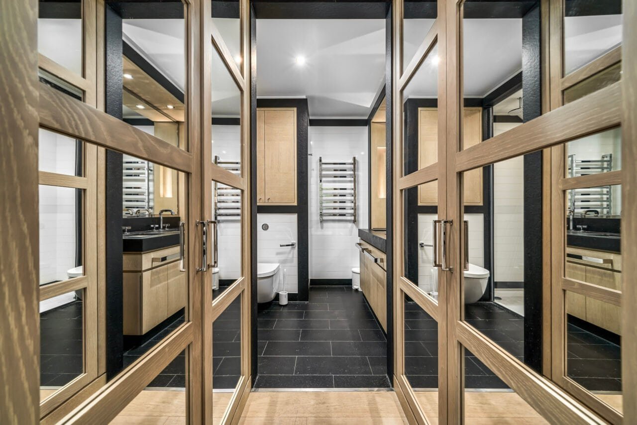 A modern public restroom with wooden partitions and black tiled flooring.