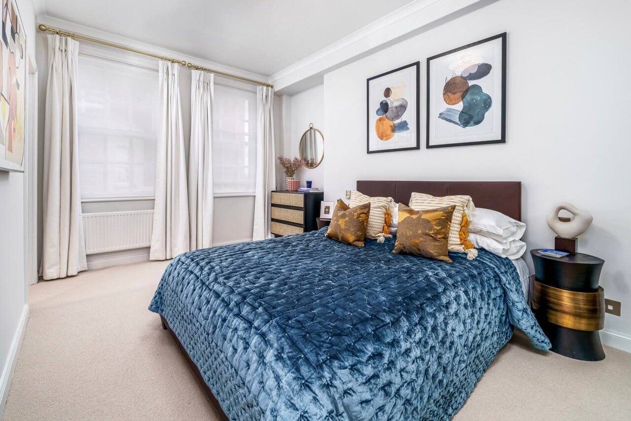 Modern bedroom with blue velvet bedspread, abstract art, and natural light.