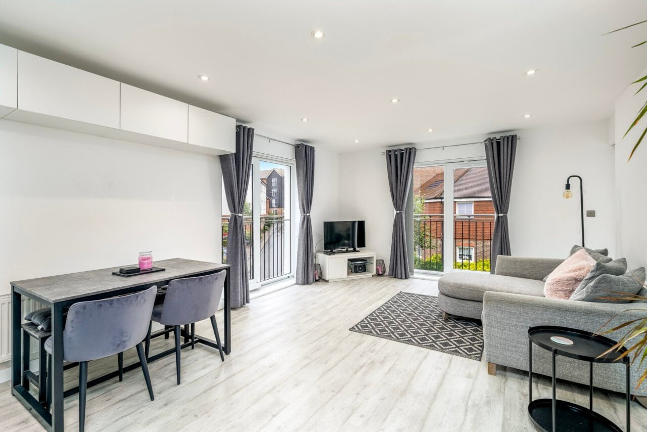 A spacious modern living room with large windows, grey sofa, and dining area.