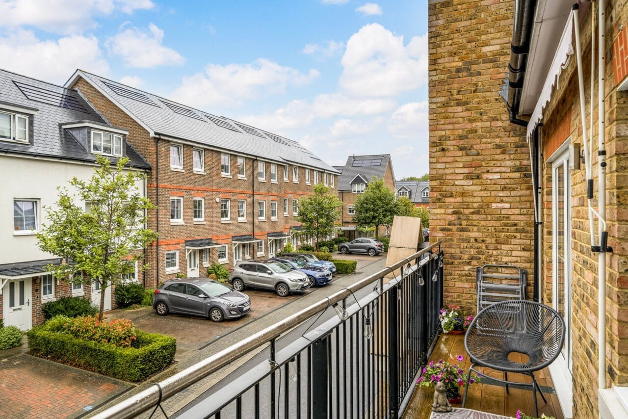 A balcony view of residential buildings with parked cars and greenery in a UK neighbourhood.