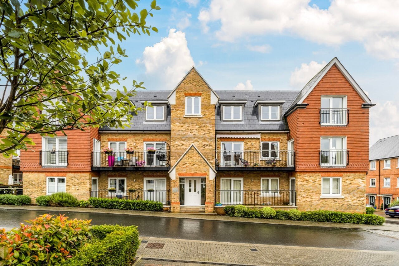 A lush residential apartment building with balconies and landscaped garden in a suburban setting.