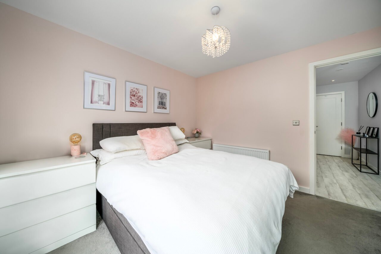 A comfortable bedroom with pink walls, white bedding, and modern decor.
