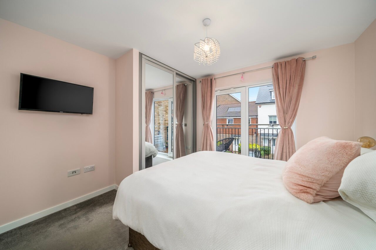 A detailed bedroom with a large bed, pink curtains, and a wall-mounted TV, overlooking a balcony.