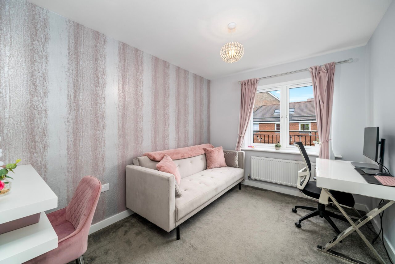 A comfortable living room with a sofa, desk, and window with pink curtains.