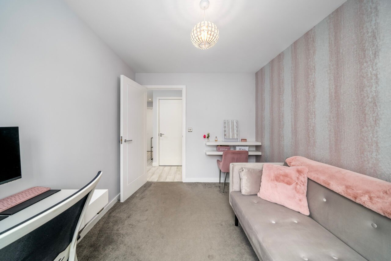 A modern living room with grey sofa, pink cushions, and minimalist decor.