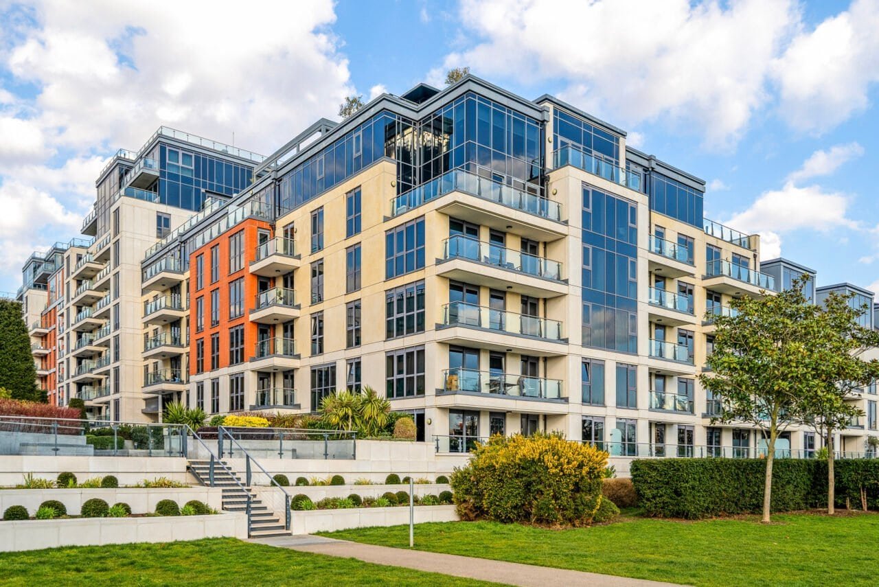 Modern multi-storey residential apartment building with glass balconies and landscaped garden.