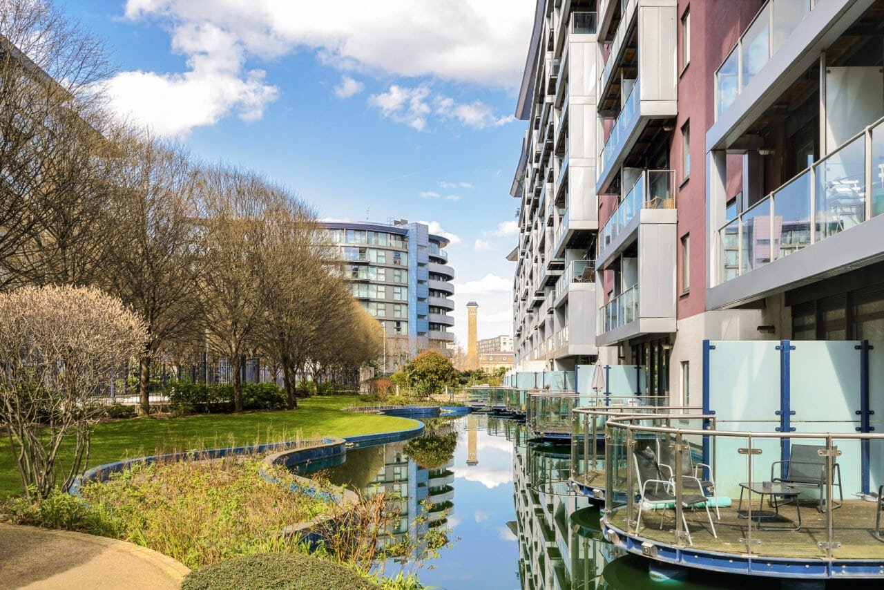 A modern riverside apartment building with balconies and outdoor seating in an urban setting.