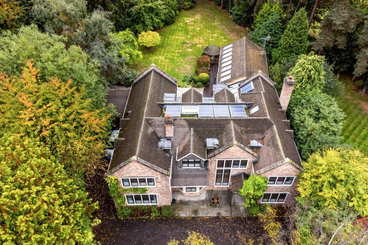 Aerial view of a large detached house surrounded by lush greenery and mature trees in a garden setti.