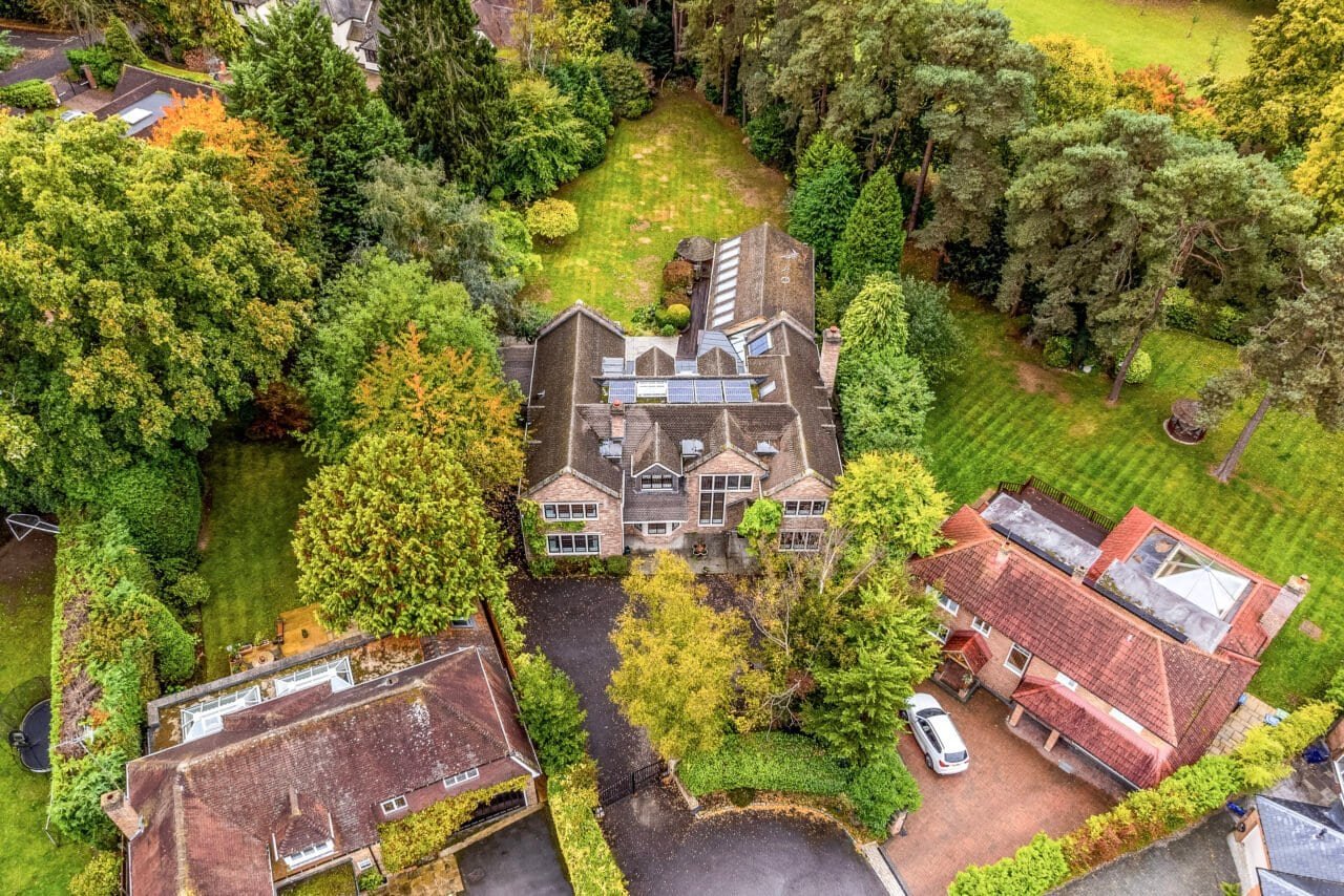 Aerial view of a large detached house with surrounding garden and trees in the UK.