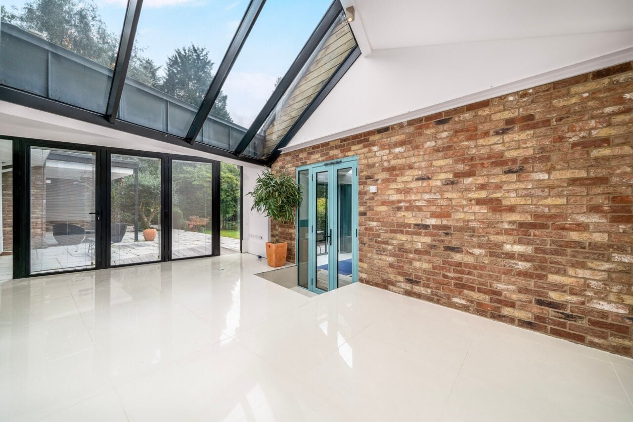 Bright modern conservatory with large glass windows and brick wall interior.