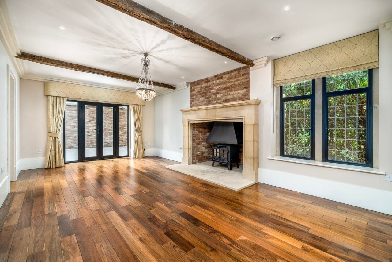 A cosy living room with wooden flooring, fireplace, and large windows with curtains.