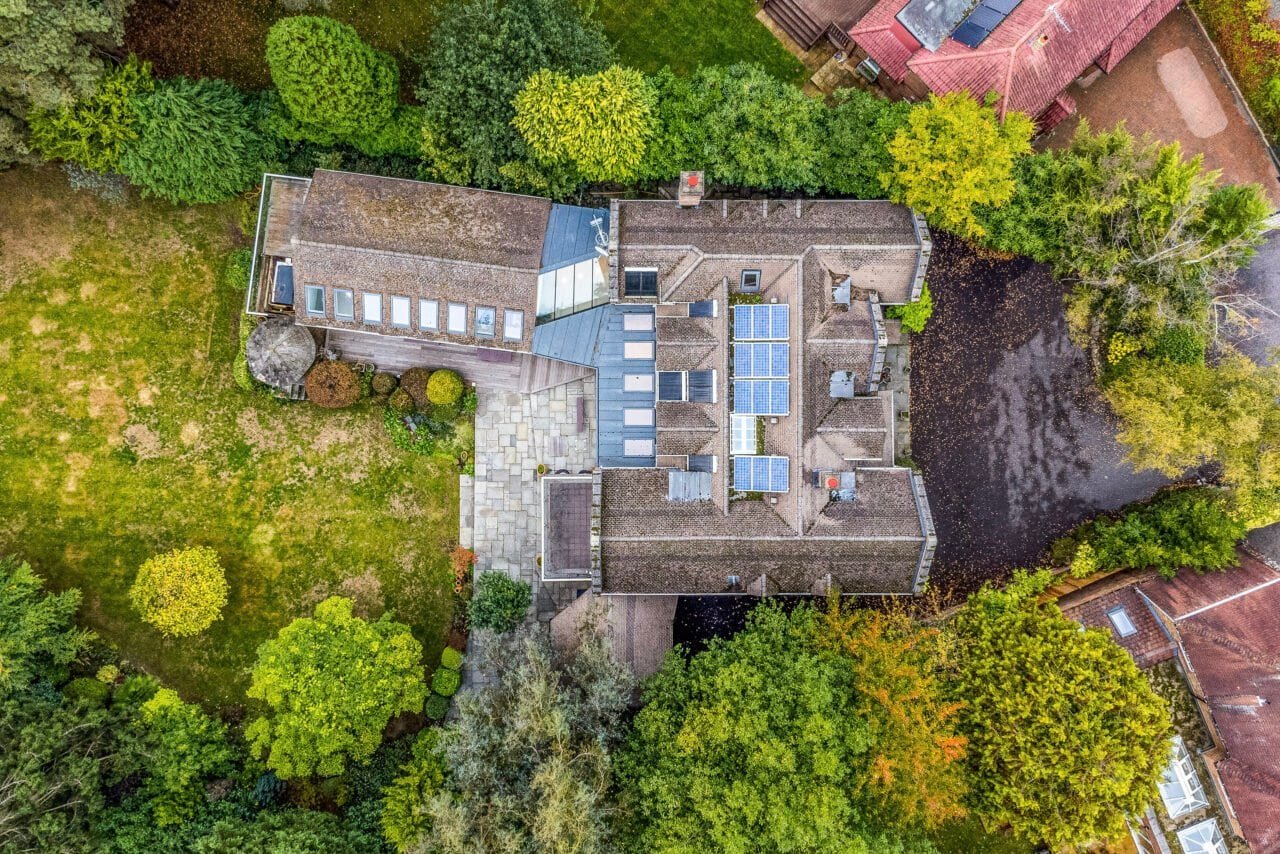 Aerial view of a large residential house surrounded by trees and garden greenery.