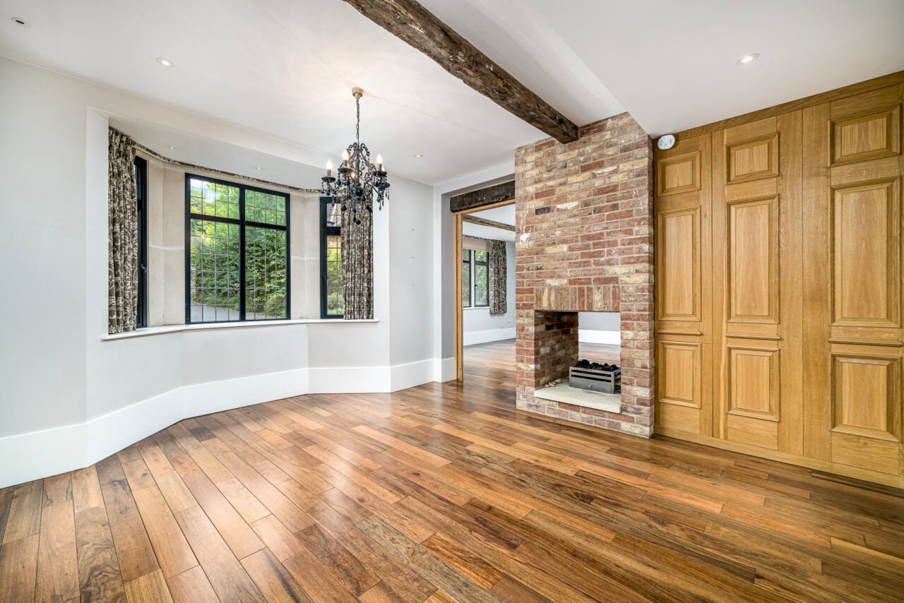Bright living room with large bay window, wooden flooring, brick fireplace, and built-in wooden cabi.