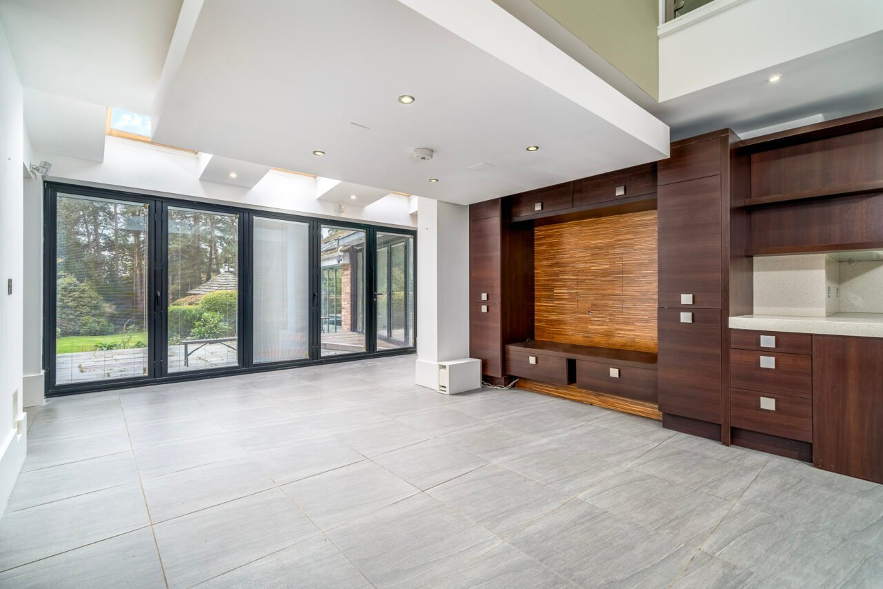 Modern living room with large glass doors, wooden wall panel, and tiled flooring.