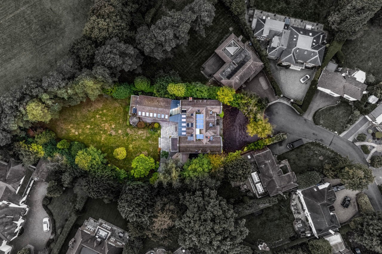 Aerial view of a modern house surrounded by trees and neighbouring properties in a residential area.