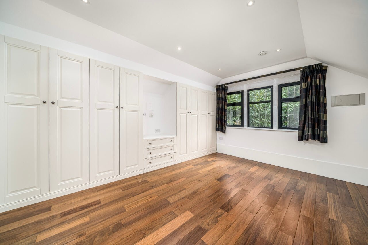 A spacious, bright bedroom with white built-in wardrobes and large windows, wooden flooring.