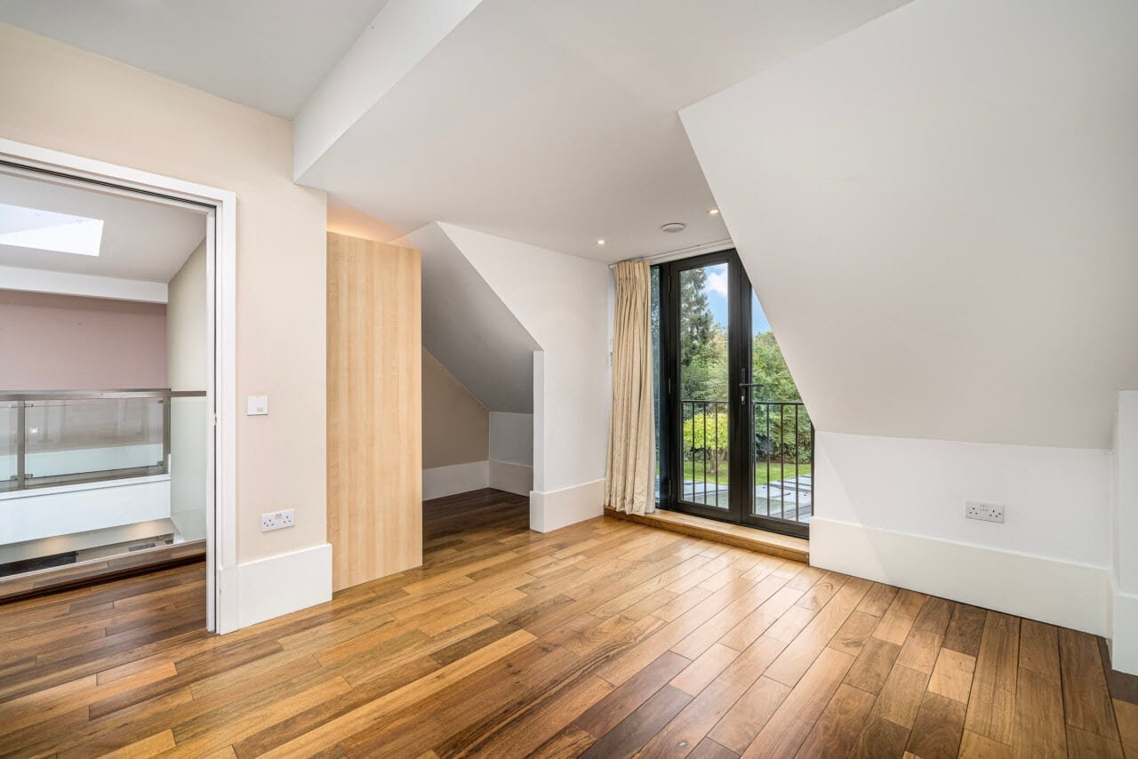 A spacious modern attic room with wooden flooring and large balcony doors.