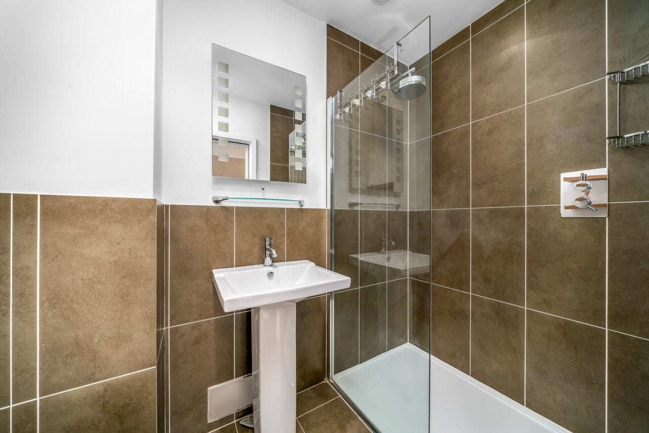 A modern bathroom with brown tiled walls and a glass shower enclosure.