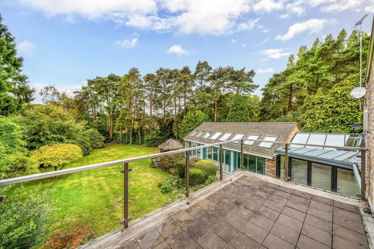 A spacious balcony overlooking a lush green garden with trees and a glass conservatory.