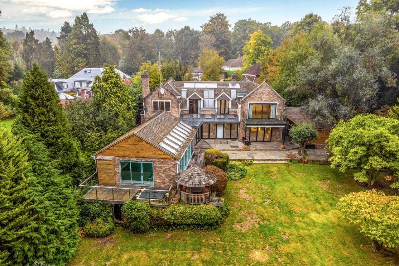 Aerial view of a modern detached house with large garden and surrounding trees in the countryside.