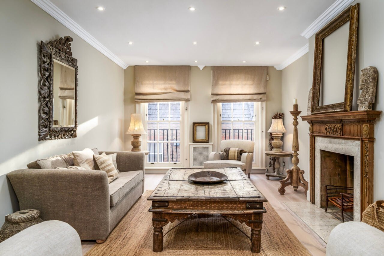 A cosy living room with beige sofas, wooden coffee table, fireplace, and large windows.